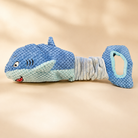 Blue and gray textured dog toy shaped like a whale on a beige background