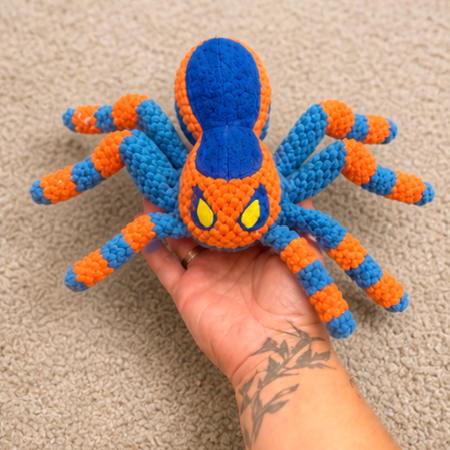 Hand holding a blue and orange spider toy on a beige carpet