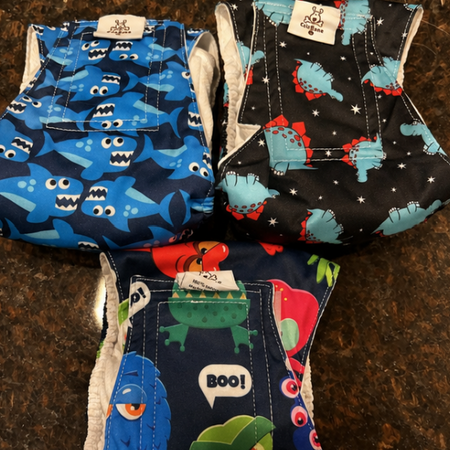 Two baby diapers with dinosaur and ghost patterns on a brown surface