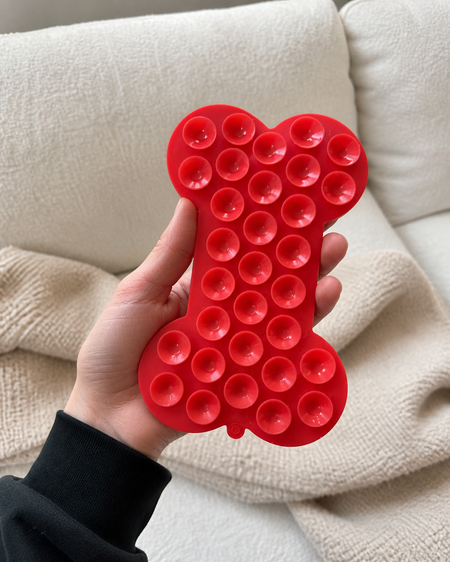 Red bone-shaped fidget toy held in a hand against a beige couch.