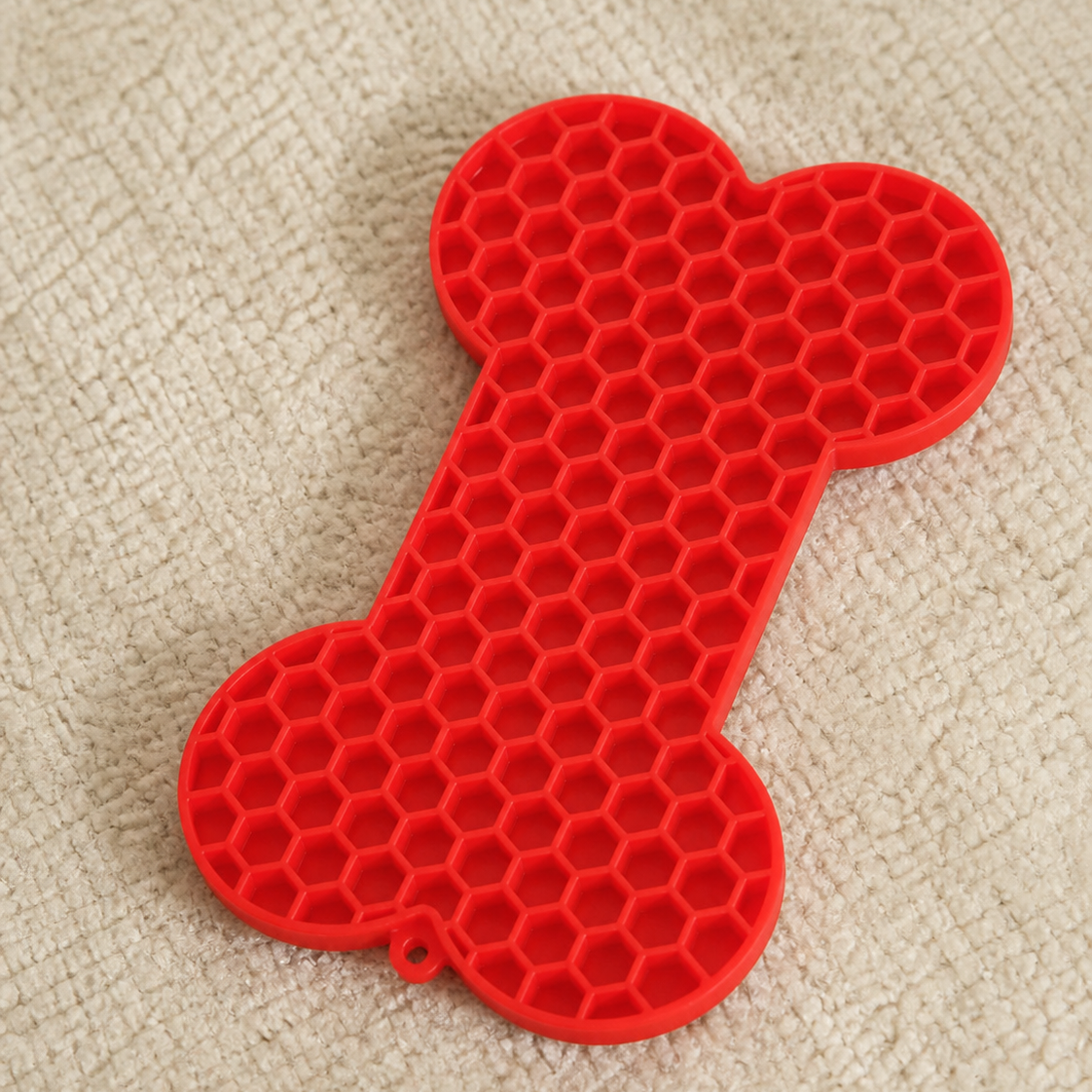 Red silicone mat shaped like a bone on a beige carpet