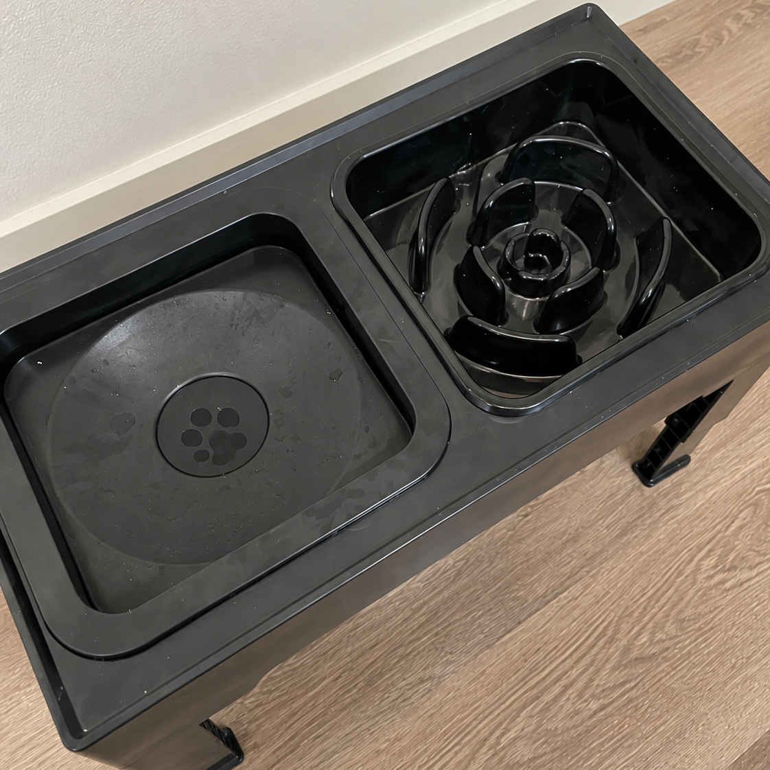 Black pet food and water bowl system on a wooden floor